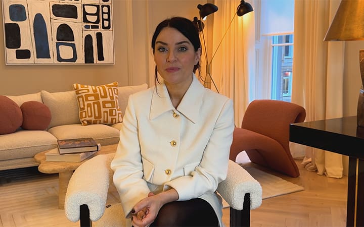 Dr. Rhona Cameron seated in a modern, softly lit living room setting, wearing a white jacket and facing the camera.