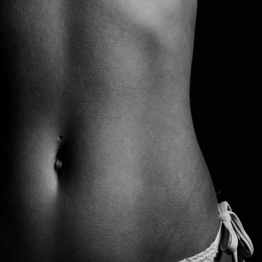 Close-up side view of a woman’s abdomen and hip showing toned, natural contours.