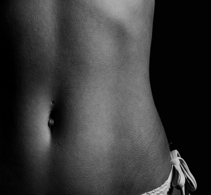 Close-up side view of a woman’s abdomen and hip showing toned, natural contours.