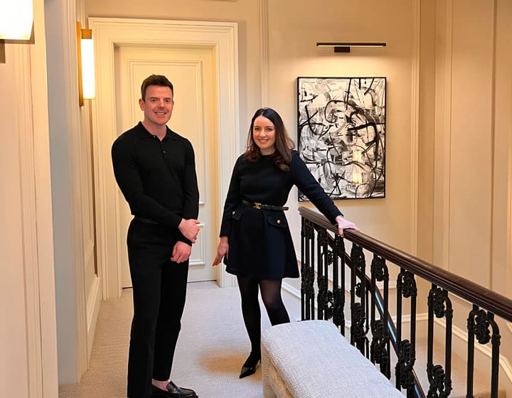 Male and female practitioners standing in a stylish clinic hallway with artwork and decorative railing in the background.